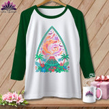 White raglan shirt with a colorful volcano graphic featuring ghosts and tropical plants.