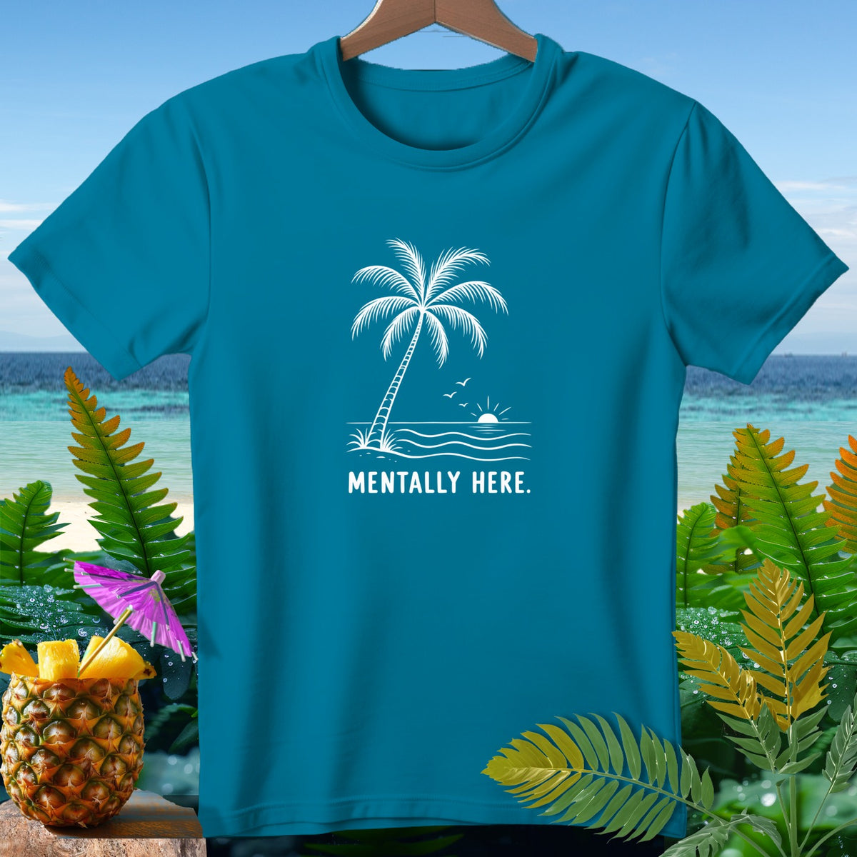 Teal t-shirt with white palm tree, waves, sun, and "MENTALLY HERE." text.