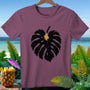 Plum t-shirt with a black monstera leaf graphic and tropical background.