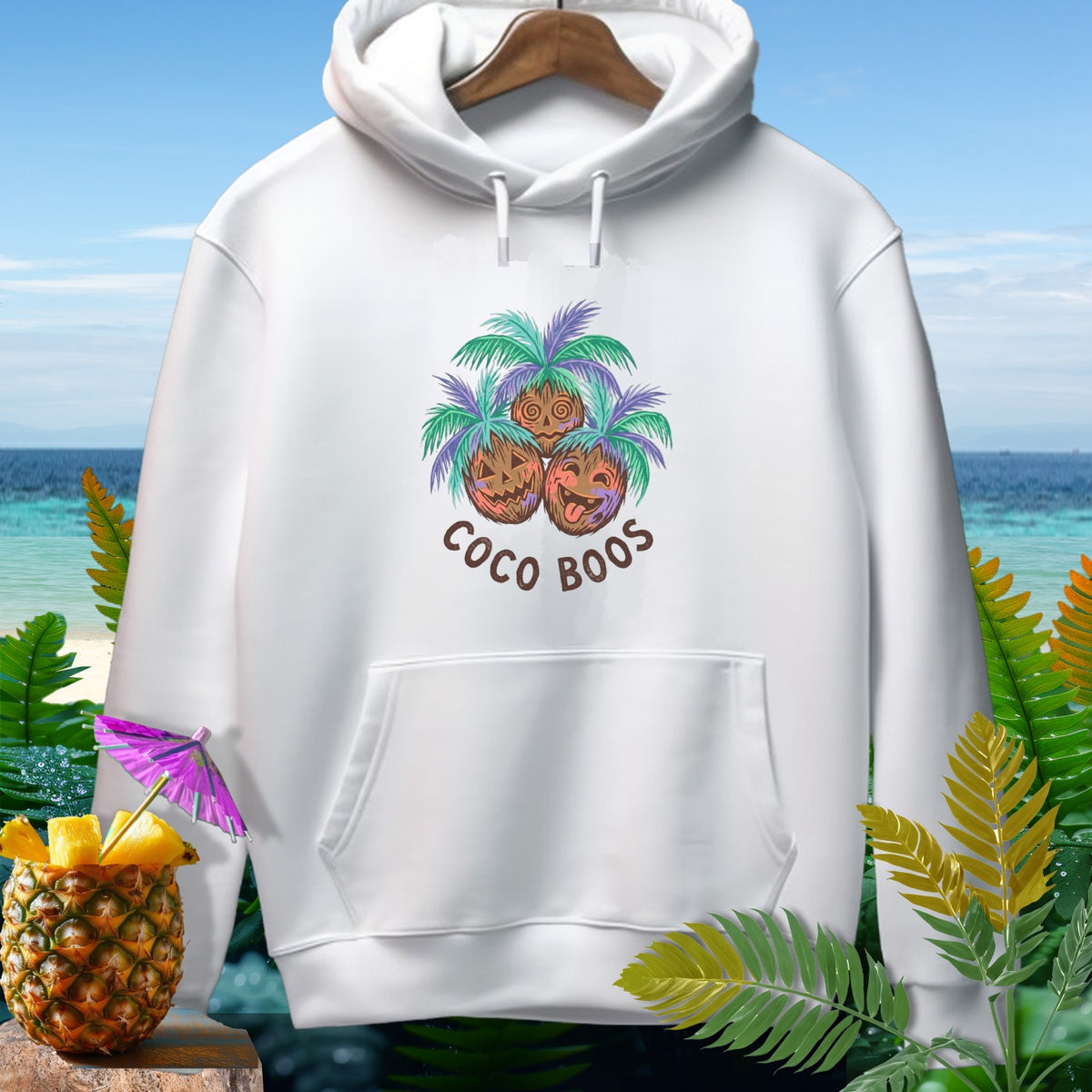 White hoodie with a "Coco Boos" graphic featuring three jack-o'-lantern coconuts and palm fronds.