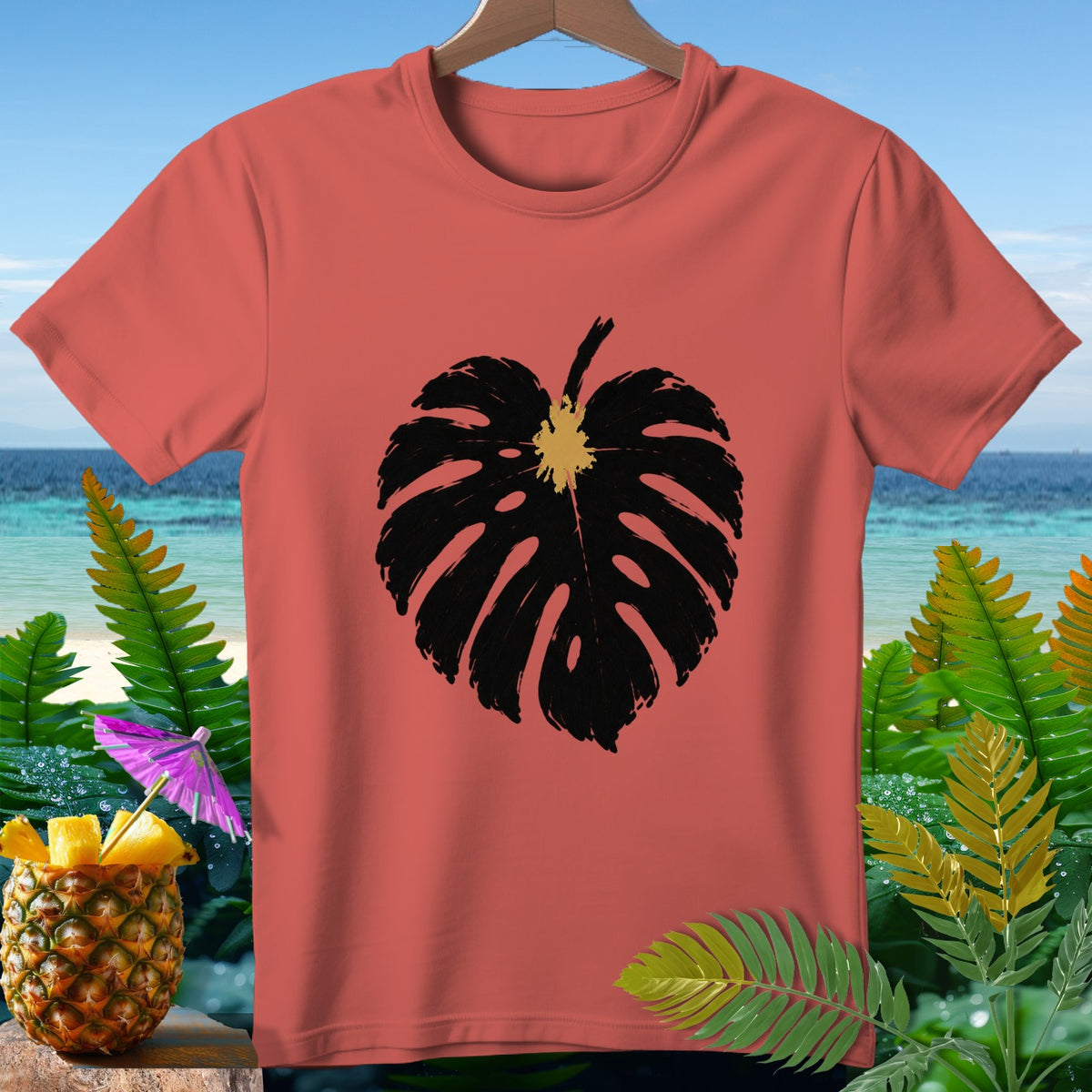 Coral t-shirt with black monstera leaf graphic and tropical background.