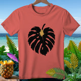 Coral t-shirt with black monstera leaf graphic and tropical background.