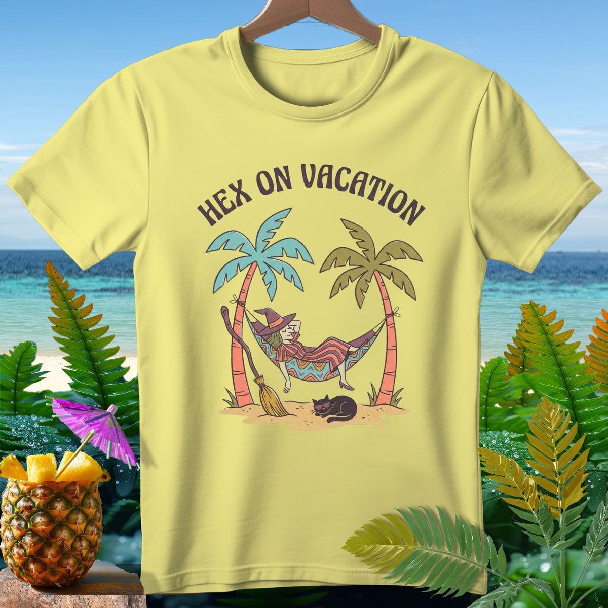 Yellow t-shirt graphic of witch in hammock with text "HEX ON VACATION".