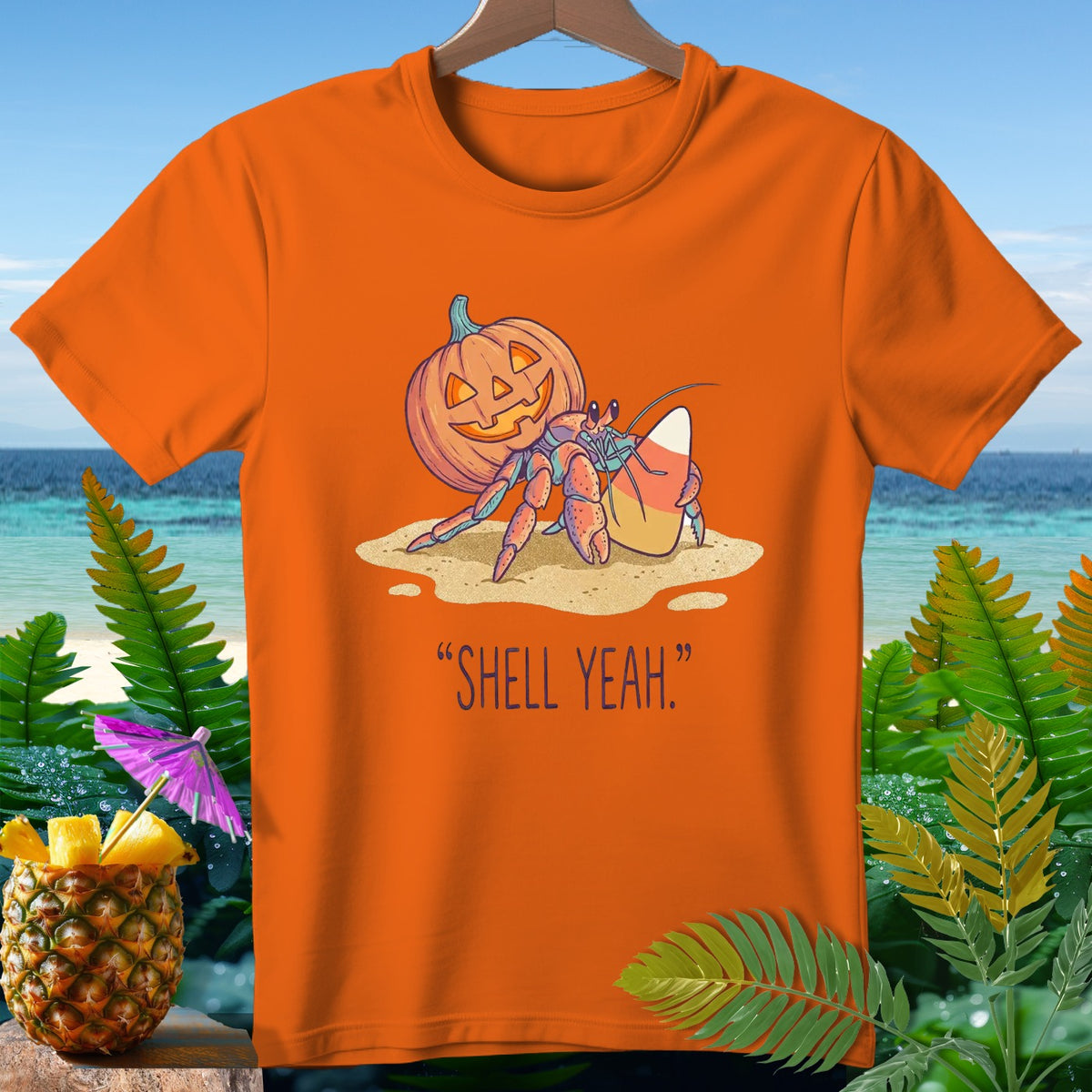 Hermit crab with pumpkin shell and candy corn on beach, text "SHELL YEAH."