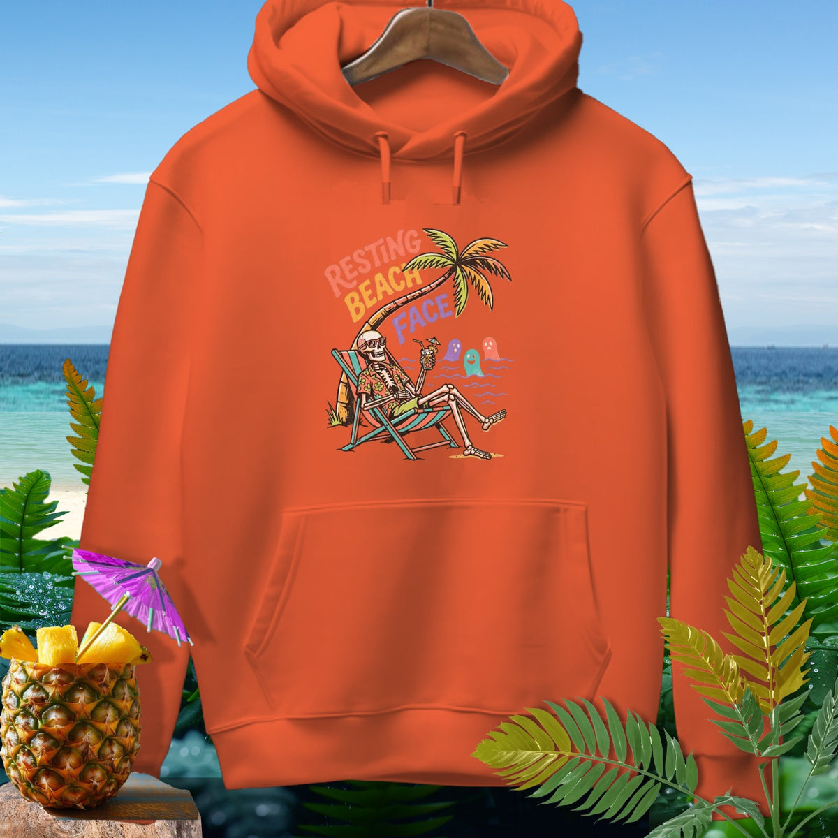 Orange hoodie with skeleton resting under a palm tree, text "Resting Beach Face".