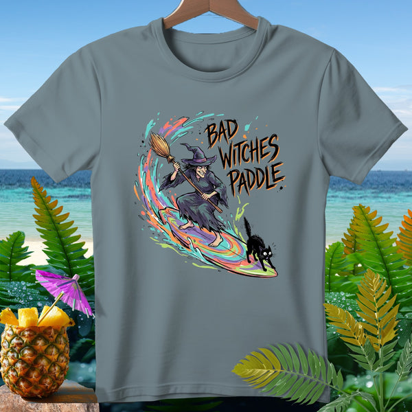 Witch surfing on a rainbow wave with a black cat, text reads "Bad Witches Paddle."