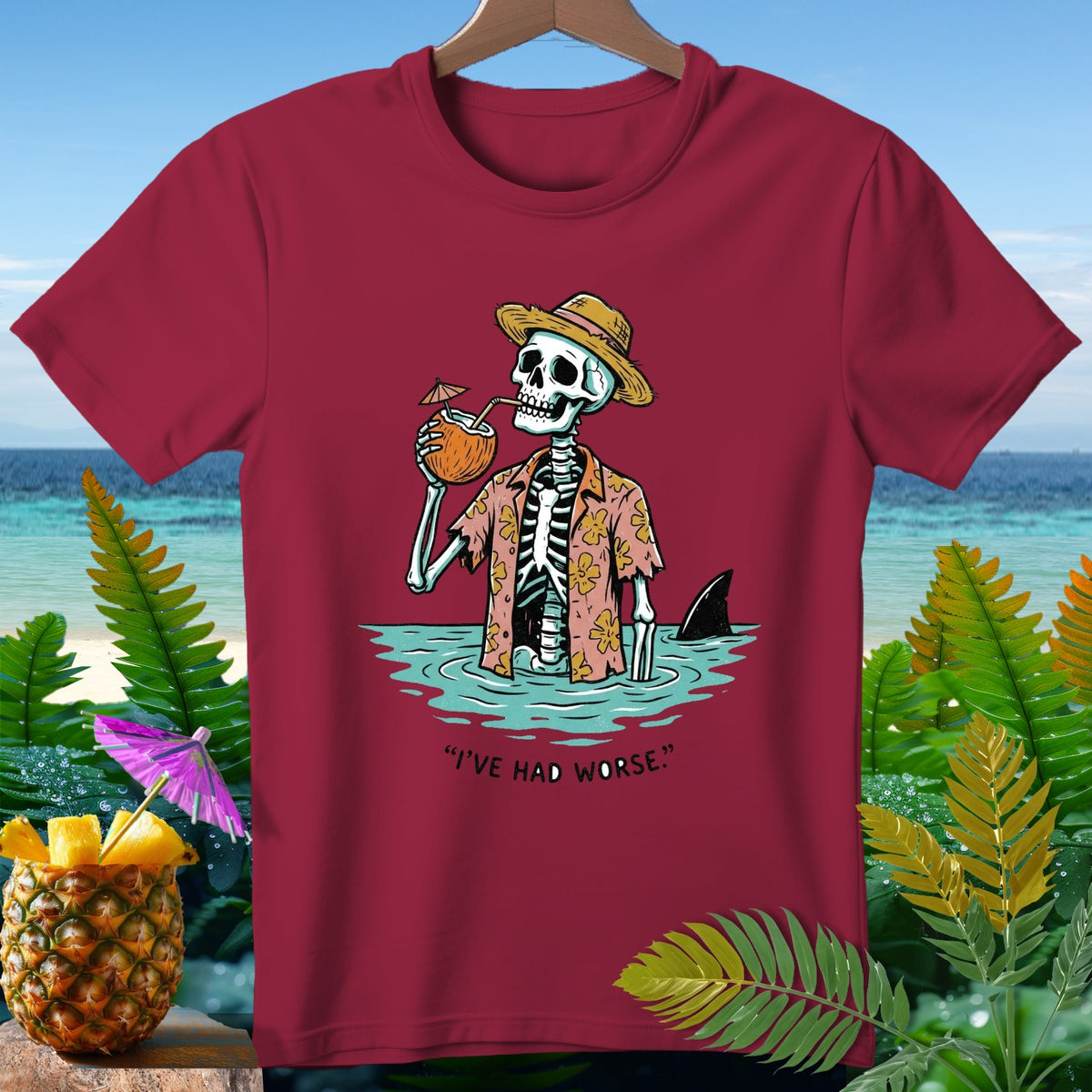 Skeleton in Hawaiian shirt drinks coconut, shark fin visible. "I'VE HAD WORSE."