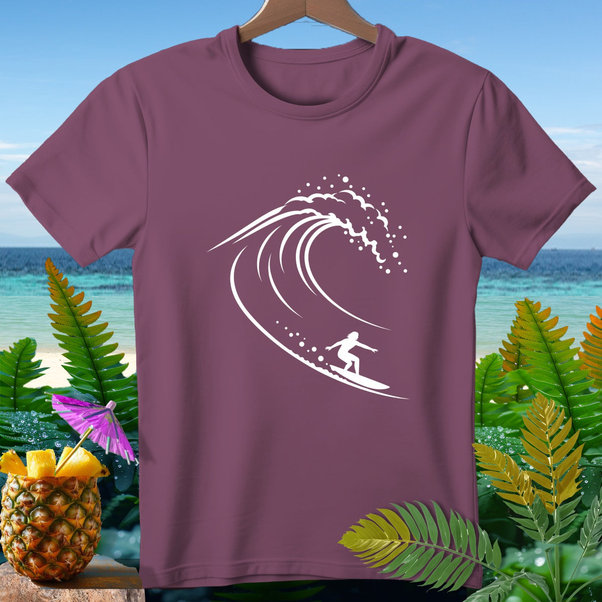Maroon t-shirt with white surfer and wave graphic, set against tropical beach backdrop.
