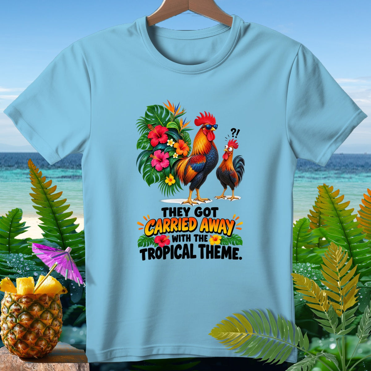 Light blue t-shirt with two roosters, tropical flowers, and the text "THEY GOT CARRIED AWAY WITH THE TROPICAL THEME."