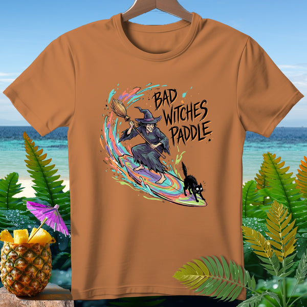 Brown t-shirt with a witch and black cat surfing on a rainbow wave, text reads "BAD WITCHES PADDLE".