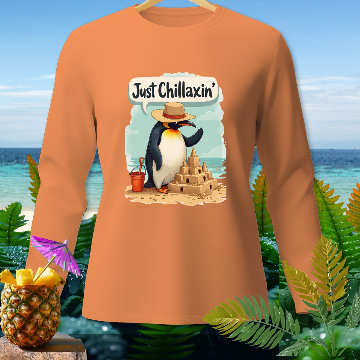 Orange long-sleeve shirt featuring a penguin building a sandcastle with "Just Chillaxin'" text.