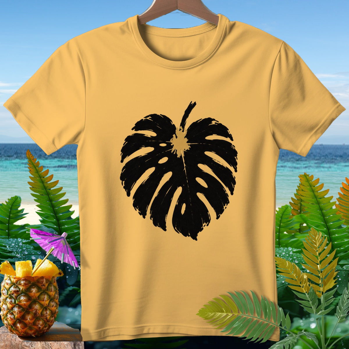 Yellow t-shirt with black monstera leaf print on beach background.